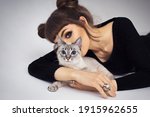 Portrait of a girl with a horn-shaped hairstyle and a blue-eyed Seal Tabby Point cat on a white background.