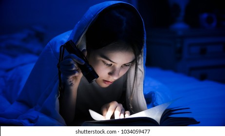 Portrait Of Girl Lying Under Blanket And Reading Scary Book