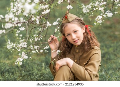 Portrait Of A Girl In Military Uniform On Victory Day On May 9 In A Blooming Garden