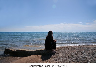 Portrait of a girl on a background of beautiful sea or lake. Girl from behind. The girl looks at the magical sea. Freedom and happiness. Kyrgyzstan. Issyk-kul Lake. Mountain lake.