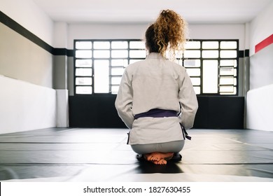 Portrait of a girl on her back kneeling on the floor mat of a gymnasium that practices martial arts like judo with lots of light in the background - Powered by Shutterstock