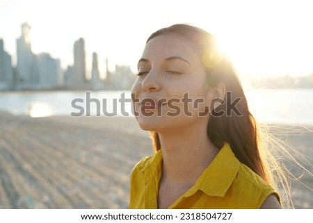 Portrait of girl on sand beach breathing fresh air at sunset with city skyline on the background