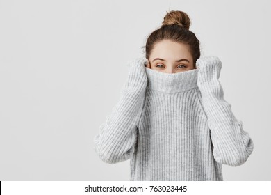 Portrait of girl pulling her trendy sweater over head having fun. Woman with tied hair in topknot being childish disappearing in her clothes looking from underneath. Happiness concept - Powered by Shutterstock