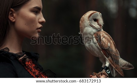 Portrait of girl in red and black dress with owl in hand. Close-up.