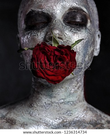Portrait of a girl in silver makeup, clay mask with a flower rose in her mouth