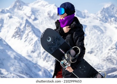 Portrait of a girl with snowboard on top of a snowy mountain.