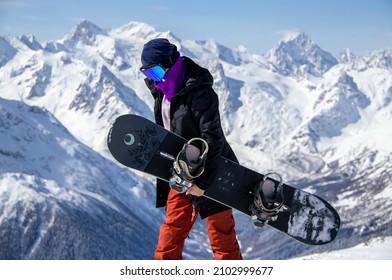 Portrait of a girl with snowboard on top of a snowy mountain.