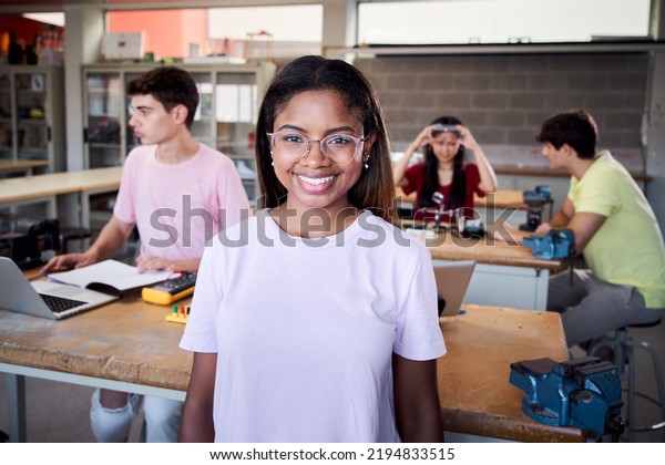 Portrait of a girl standing in a technology class\
looking at the camera. Vocational training students in the\
classroom studying electronics, robotics, electricity or some kind\
of technical college