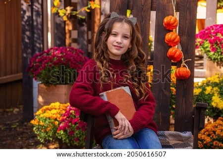 portrait of a girl in a sweater with a book reads on a bench in autumn near the house