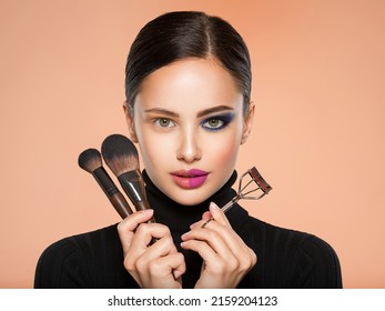 Portrait of a girl with  tools for making makeup near face.  One half face of a beautiful white woman with  bright makeup and the other is natural. Woman holds makeup brush and eyelash curler. Natural - Shutterstock ID 2159204123