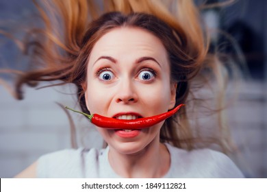 Portrait Of A Girl With A Very Hot Red Pepper In Her Mouth. The Woman Is Amazed. Round Eyes From Hot Vegetable. Proper Nutrition. Vegetarian Food. Housewife Preparing Spicy Food