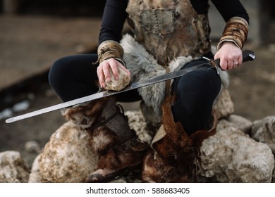 Portrait Of A Girl In A Viking Outfit, Red Hair. Sharpening The Sword