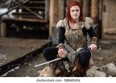 Portrait Of A Girl In A Viking Outfit, Red Hair. Sharpening The Sword