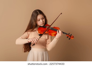 Portrait of a girl with a violin and a bow in her hands on a plain beige background. Music concept - Powered by Shutterstock