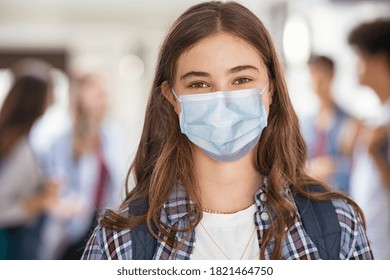 Portrait Of Girl Wearing A Face Mask Standing In College Campus And Looking At Camera. University Young Woman Smiling Despite The Covid-19 Pandemic. Satisfied And Proud Student Girl With Surgical Mask