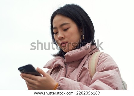 Portrait of girl in white background using her smartphone to read messages.  Browsing internet.