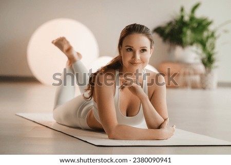 Portrait of a girl in white clothes lying on a mat before doing yoga indoors.
