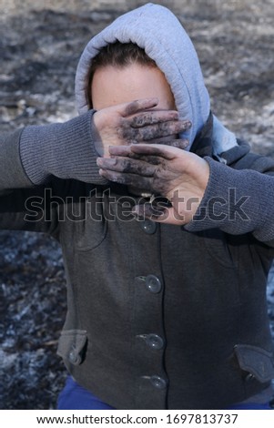 Portrait of a girl who covers her face with dirty hands. girl's hands in the ashes. girl stands in ashes
