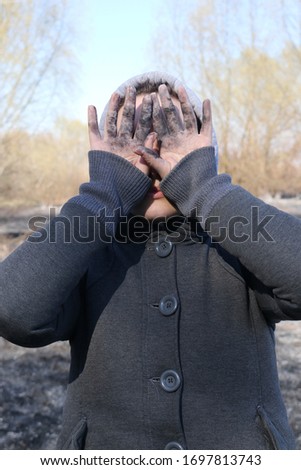 Portrait of a girl who covers her face with dirty hands. girl's hands in the ashes. girl stands in ashes
