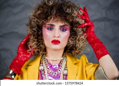 Portrait of a girl in a yellow jacket and blue jeans with afro hair of the eighties, disco era. Photo in studio on a gray background.
