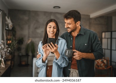 Portrait of girlfriend show mobile phone screen to her boyfriend while he drink a coffee at home - Powered by Shutterstock