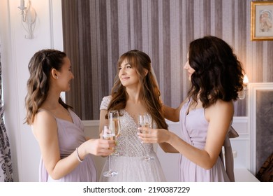 Portrait of girls, bridesmaids greeting beautiful bride in dress with lace, drinking champagne and smiling, preparing for wedding day, celebrating in apartment.