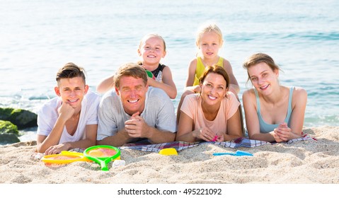 Portrait Of Glad  Family With Four Children Lying Together On Beach On Weekend