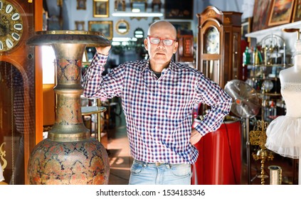 Portrait Of Glad  Positive  Successful Owner Of Antiques Shop Among Vintage Things