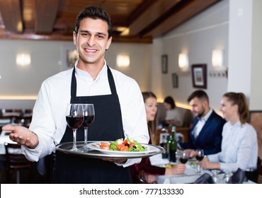 Portrait of glad smiling waiter with serving tray meeting restaurant guests