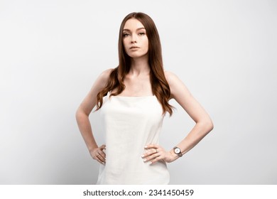 Portrait of glamorous serious woman with long hair wearing nightgown with watch on hand, posing on gray background. Attractive girl waiting, looking at camera. Fashion model concept