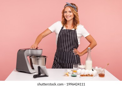 Portrait of good looking female confectioner preparing ingredients for baking, looking at camera with smile, being happy to use new food processor. Indoor studio shot isolated on pink background. - Powered by Shutterstock