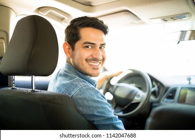 Portrait Of Good Looking Young Hispanic Man Sitting In The Driving Seat Of The Car And Looking Back With A Smiling Face