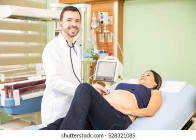 Portrait Of A Good Looking Young Hispanic Obgyn Examining A Pregnant Woman In A Hospital Room