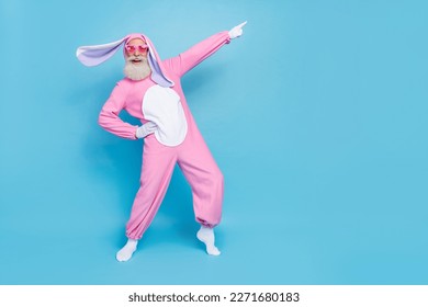 Portrait of good mood elderly pensioner wear pink bunny costume indicating empty space hand on waist isolated on blue color background