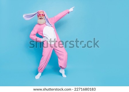 Portrait of good mood elderly pensioner wear pink bunny costume indicating empty space hand on waist isolated on blue color background