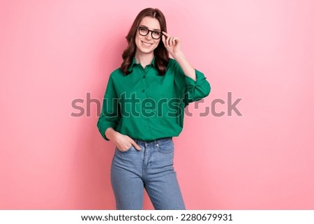 Portrait of good mood lovely smart girl curly hairstyle wear green shirt arm in pocket touching glasses isolated on pink background