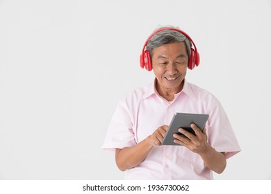 Portrait Of A Good-looking Full Of Energy And Active Senior Older Asian Man Holding And Wearing Red Headphone And Listening To Music Via Tablet Computer With Joyfully And Happy On White Background.