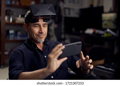 Portrait Of A Good-looking Happy Older White Man Using VR Glasses And Smart Phone At Home, Indoors.