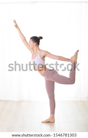 Portrait of gorgeous active sporty young woman practicing yoga in studio. Beautiful girl practice Dandayamana Dhanurasana, standing bow pulling pose. Healthy active lifestyle, working out in gym.