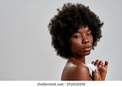 Portrait Of Gorgeous African American Female Model With Afro Hair Touching Her Perfect Glowing Skin With White Feather, Posing Isolated Over Gray Background. Skin Care, Diversity Concept