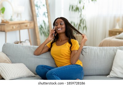 Portrait Of Gorgeous Black Woman Speaking On Mobile Phone And Smiling While Relaxing On Sofa At Home. Cheerful African American Lady Discussing News With Her Family Or Friends On Cellphone