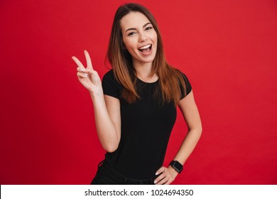 Portrait Of Gorgeous Brunette Woman Looking At Camera With Smile And Showing Peace Sign With Fingers Isolated Over Red Background