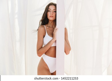 Portrait of gorgeous caucasian woman in swimsuit standing over white curtains at beach summer resort - Powered by Shutterstock