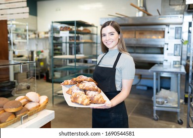 Portrait of a gorgeous female baker holding a tray of delicious sweet bread in a bakery shop - Powered by Shutterstock