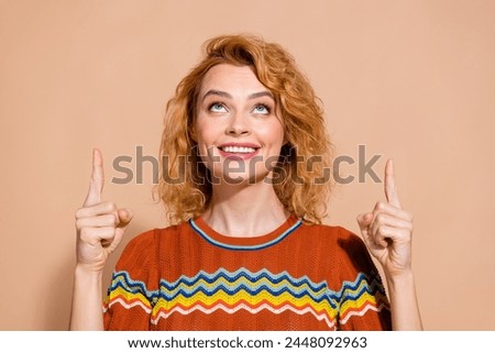 Portrait of gorgeous girl with foxy hair wear knit t-shirt directing look up at logo empty space isolated on beige color background