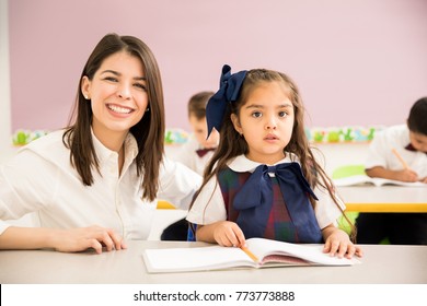 Portrait Of A Gorgeous Hispanic Preschool Teacher Helping One Of Her Students In The Classroom