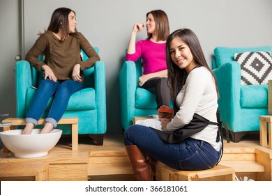 Portrait Of A Gorgeous Hispanic Young Woman Working At A Nail Spa And Giving A Pedicure To A Couple Of Women