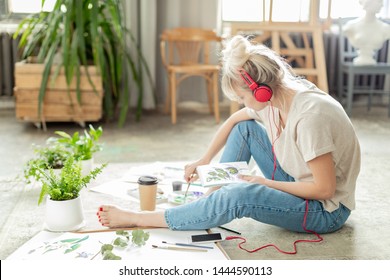 Portrait of gorgeous original female holding painting brush in hands and trying to sketch beautiful living sprout on paper with watercolor. Arts and crafts concept