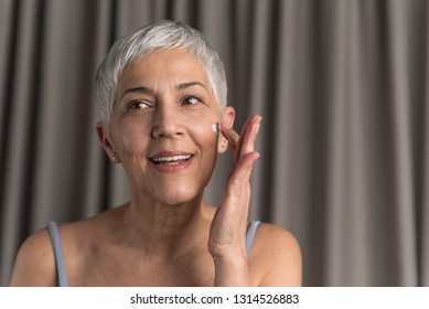 Portrait Of Gorgeous Senior Woman Smearing Anti Age Cream With Q10 On Her Face, Anti Wrinkle Cosmetic And Selfcare Concept