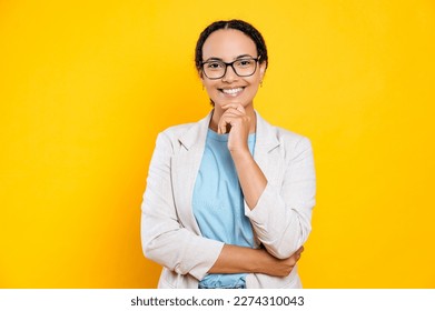 Portrait of a gorgeous successful mixed race business woman with glasses, stylishly dressed, hr manager, real estate agent, broker, looks at camera, smiles, stands on isolated yellow background - Shutterstock ID 2274310043